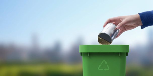 Woman putting a tin in the trash bin, waste sorting and recycling concept - 写真・画像