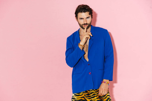 Young man wearing blue jacket showing silence gesture at camera isolated over pink background - Фото, зображення