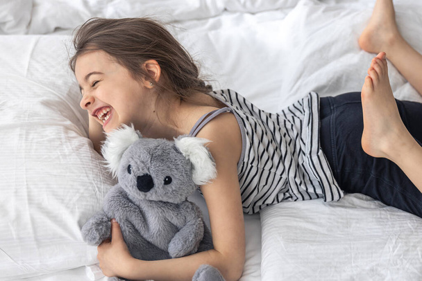 Ευτυχισμένο κοριτσάκι με μαλακό παιχνίδι κοάλα στο κρεβάτι. - Φωτογραφία, εικόνα