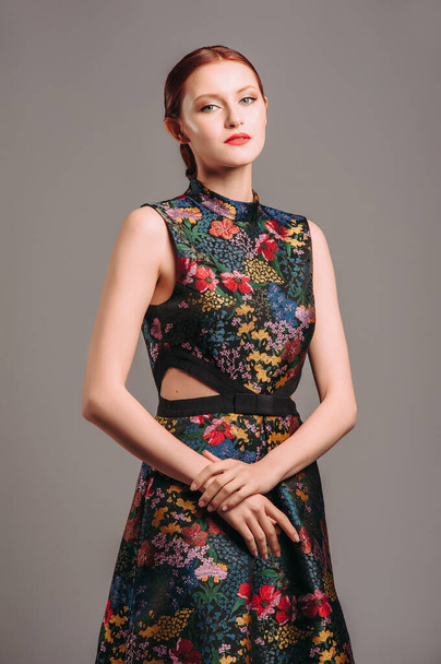Cut out waist midi dress in floral embroidery with black high heels. Ginger lady posing in studio. Evening colourful sleeveless gown with high neck line, female fashion, gorgeous chic look. - Foto, Imagen