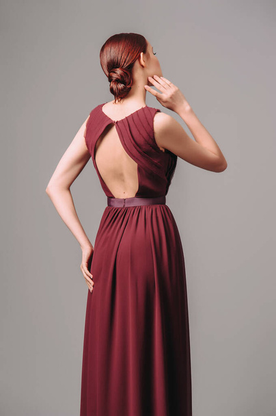 Valentine's day romantic outfit. Burgundy chic gown. Red cocktail sleeveless dress with rounded neckline and back details. Sensual young ginger lady. Studio shot.  - Fotó, kép