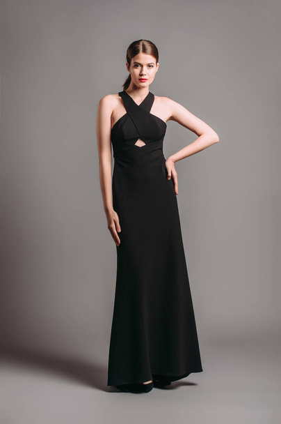 Criss-cross fitted maxi dress in black. Sleeveless open-back sexy evening gown. Beautiful young lady posing in studio. Elegant female fashion, summer festive look. - Foto, imagen