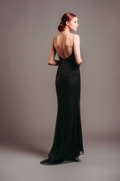 Black evening dress. Elegant lady in full-length backless sleeveless vintage gown with straps. Studio portrait of a beautiful young woman, gorgeous look. Female fashion - Foto, immagini