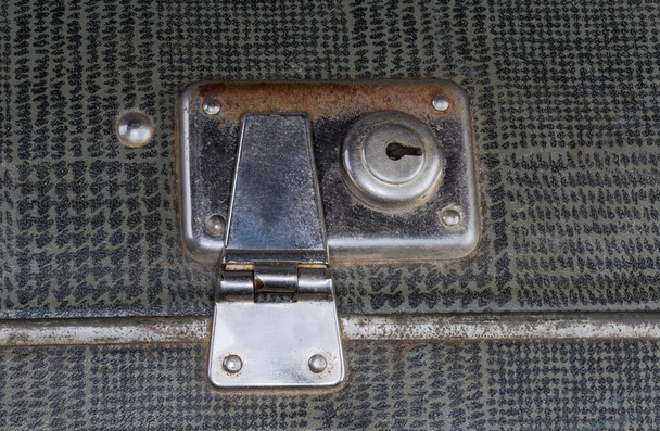 Metal partly rusty inbuilt lock of the closed old fashioned shabby gray leatherette hardshell suitcase, close-up - Photo, image