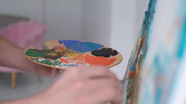 Close-up van een kunstenaarshand die een penseel vasthoudt en een tekening maakt met veelkleurige verf. - Foto, afbeelding
