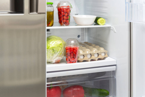 An open fridge in the house with shelves full of vegetables - Фото, изображение