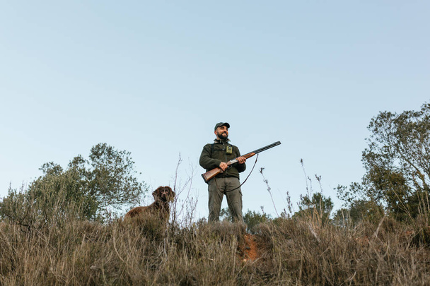 Hunter κρατώντας το όπλο του στέκεται χαμογελώντας κοιτάζοντας μακριά στη φύση - Φωτογραφία, εικόνα