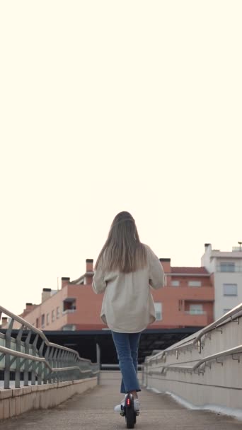 Rückwärtsblick einer jungen Frau, die nachmittags nach der Schule mit dem E-Roller unterwegs ist - Filmmaterial, Video