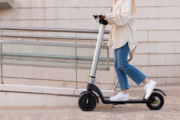 Half cropped view of young unrecognizable woman riding an electric scooter around the city center with buildings around - Foto, Imagen