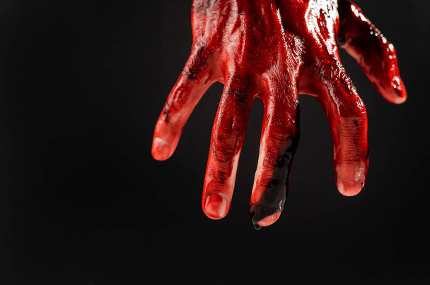Primer plano de una mano masculina manchada de sangre sobre un fondo negro.  - Foto, imagen