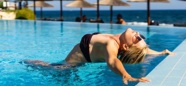 Νεαρή γυναίκα χαλαρώνει στην πισίνα στις καλοκαιρινές διακοπές. Ξανθιά, καυκάσια. - Φωτογραφία, εικόνα