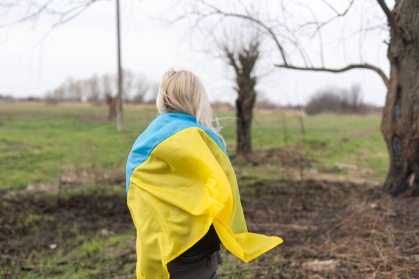 Жінка тримає жовтий і синій прапор України на тлі обгорілого дерева. - Фото, зображення