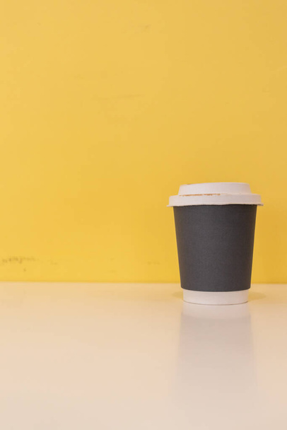 Paper coffee mugs filled with hot coffee are placed on a table in a cafe on a bright yellow blur background, there is space in the image for design and copy space for inserting text for advertising. - Zdjęcie, obraz
