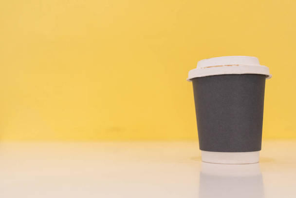 Paper coffee mugs filled with hot coffee are placed on a table in a cafe on a bright yellow blur background, there is space in the image for design and copy space for inserting text for advertising. - Photo, Image
