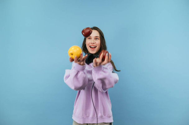 Positieve jonge brunette vrouw jongleren appels met glimlachen op haar gezicht - Foto, afbeelding