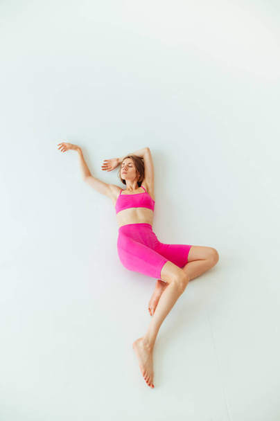 Beautiful sporty blonde woman in pink sportswear lies on a white background. Vertical - Fotó, kép