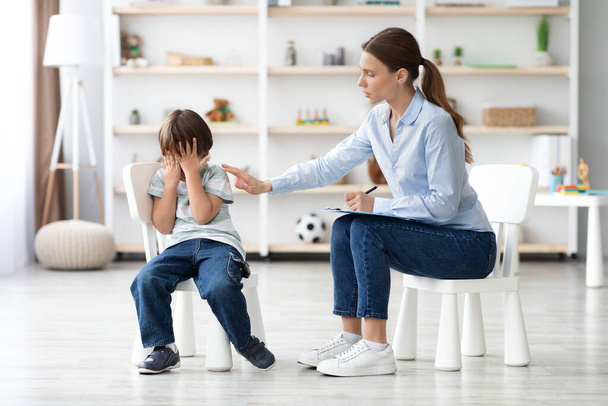 deprimovaný malý chlapec pláče během psychologické sezení s profesionálním terapeutem, starostlivá žena ho utěšuje - Fotografie, Obrázek