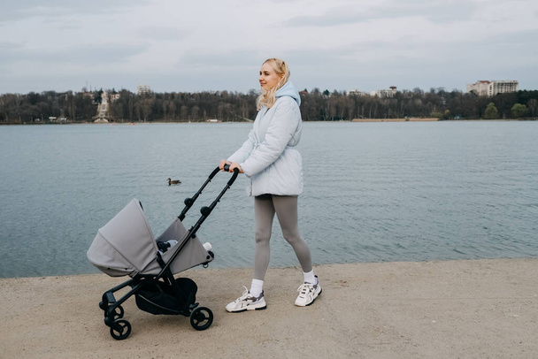 Blonde woman walking with a stroller by the lake in springtime.  - Zdjęcie, obraz