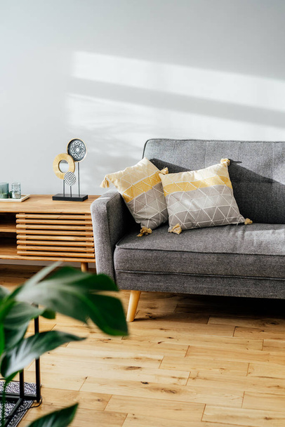 Stylish living room interior with designer console with decor and gray sofa with graphic pillows. White walls, green plants in the pots. Light wooden oak parquet. Modern Scandinavian style interior. - Fotoğraf, Görsel