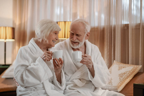 A senior couple in white robes having coffee and talking - Foto, Imagem
