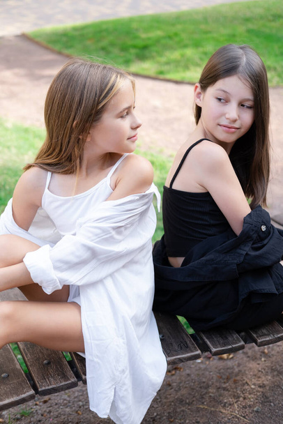 Broederlijke tweeling zussen. blonde en brunette tienermeisjes in modieuze zwart-wit kleding buiten. zusterschap, broers en zussen die samen tijd doorbrengen - Foto, afbeelding