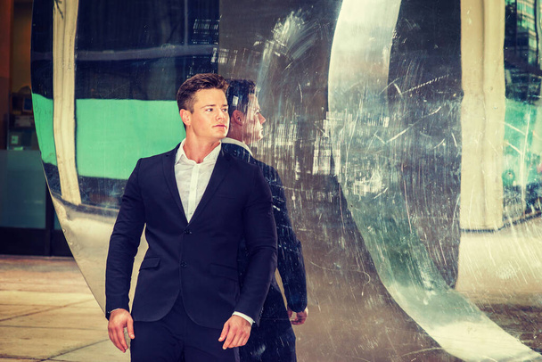 Portrait of Successful American Businessman. Dressing in black suit, a young, strong, sexy guy standing by metal mirror wall, looking away, confidently looking forward. - Photo, Image