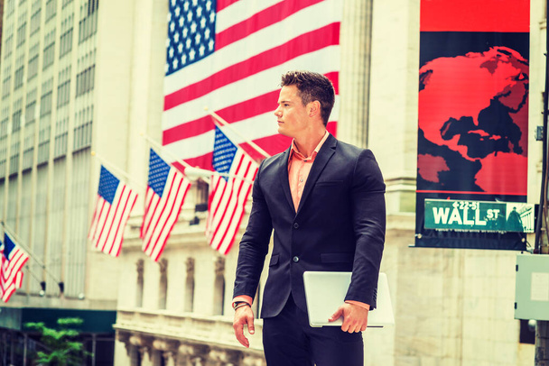 Гордий американський бізнесмен 4 липня, День незалежності, в Нью-Йорку. Одягаючись у чорний костюм, тримаючи портативний комп'ютер, молодий, сильний, сексуальний хлопець стоїть на Уолл-стріт. Американський прапор на тлі - Фото, зображення