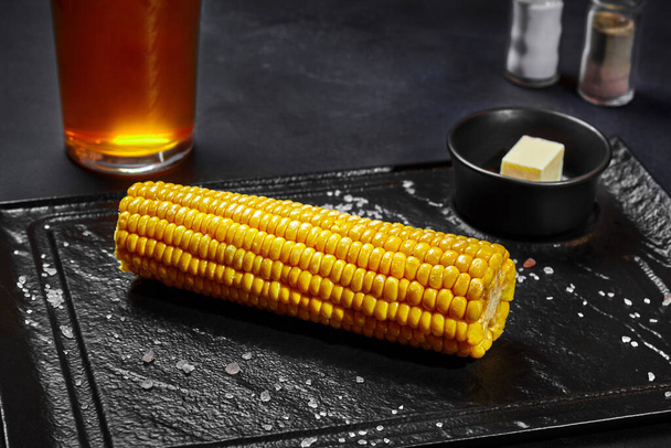 Приготовленное ухо сладкой кукурузы с солью и маслом на черной доске - Фото, изображение