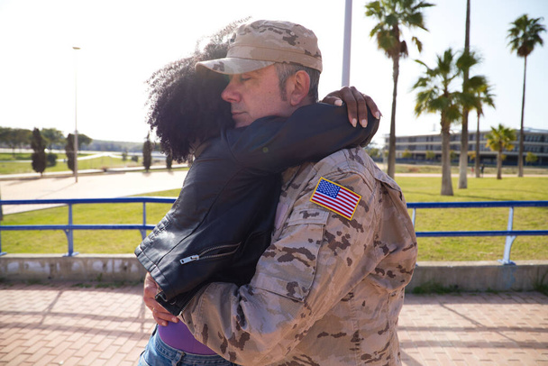 Afroamerykańska kobieta i amerykański żołnierz, którzy właśnie przybyli z wojny na misję pokojową, mocno się przytulają. Kobieta jest szczęśliwa. Koncepcja wojny i armii, pokoju i misji. - Zdjęcie, obraz