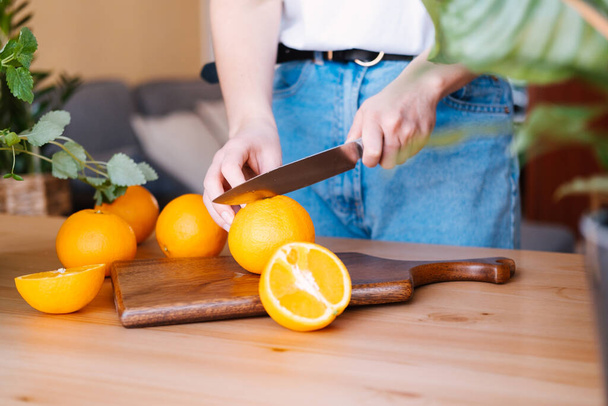 Γυναίκα κοπή πορτοκάλια σε μια κουζίνα γεμάτη φυτά. - Φωτογραφία, εικόνα