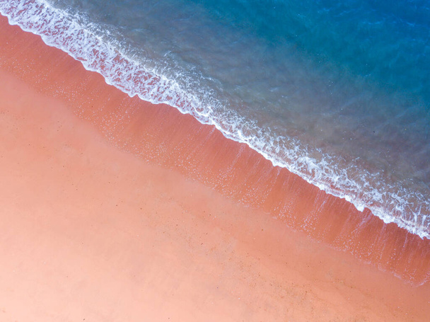 Koyu mavi deniz renginde pembe kumsal manzarası ve yaz aylarında seyahat ve tatil için fotokopi uzayıyla çarpan beyaz dalga. - Fotoğraf, Görsel
