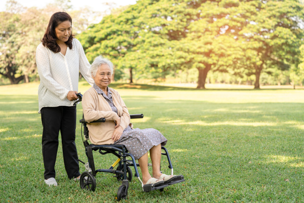 Gondozó segítséget és ellátást ázsiai idős vagy idős hölgy beteg ül tolószéken a parkban, egészséges erős orvosi koncepció. - Fotó, kép