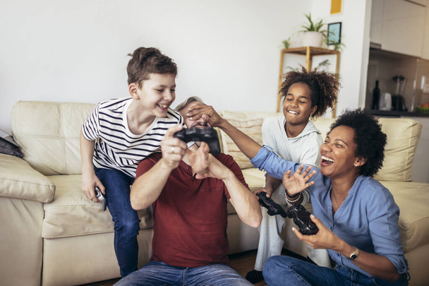 Familia sonriente disfrutando del tiempo juntos en casa sentados en el sofá en la sala de estar y jugando videojuegos. - Foto, Imagen