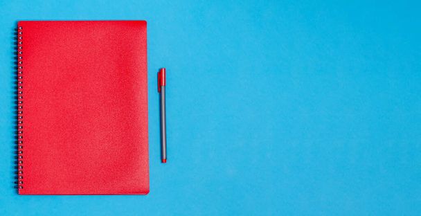 Notebook with a pen on a blue background. Concept of preparation for school, stationery. Flat lay, top view. - Fotografie, Obrázek