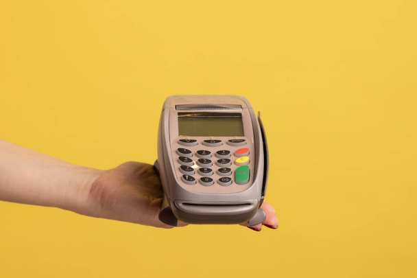 Profile side view closeup of woman hand holding and showing POS or terminal payment or pay pass device. Indoor studio shot isolated on yellow background. - Foto, Imagem