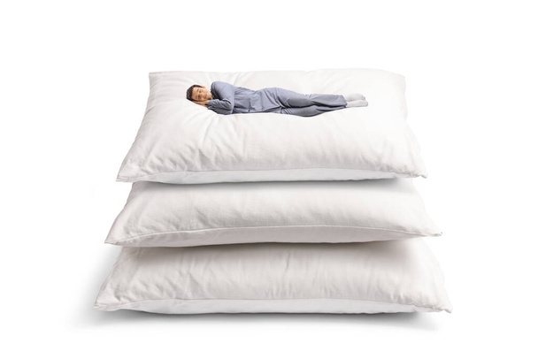 Giovane in pigiama che dorme su un mucchio di grandi cuscini isolati su sfondo bianco - Foto, immagini