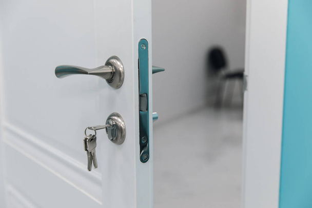 White room door with handle and key in the door loc - Foto, Bild