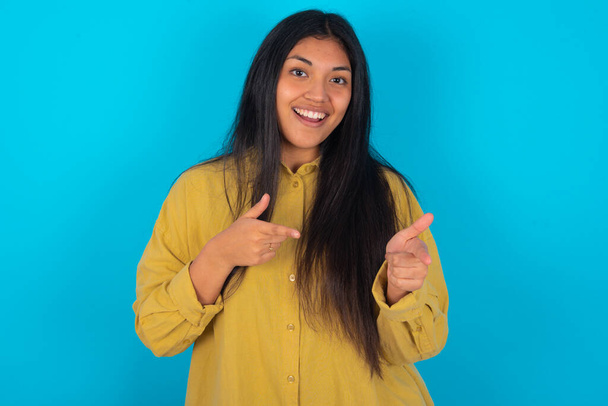 青い背景に黄色いシャツを着た若いラテン系の女性が誰かを選ぶ。君を推薦するよ。ベストチョイス - 写真・画像
