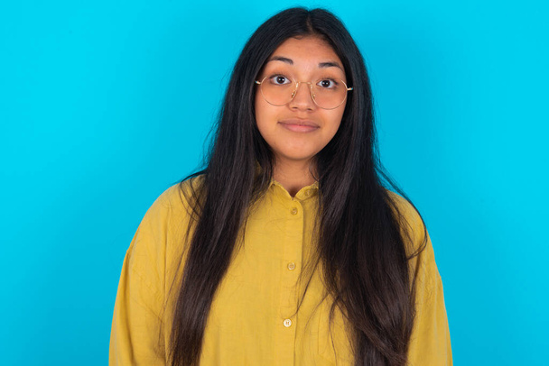 Stunned young latin woman wearing yellow shirt over blue background stares reacts on shocking news. Astonished MODEL holds breath - Photo, Image
