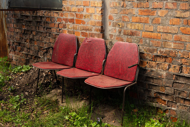 Три розбірні стільці в ряд проти червоної старої цегляної стіни
 - Фото, зображення