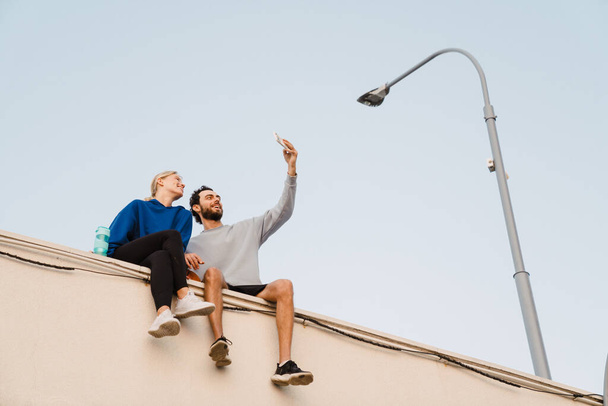 Young man and woman taking selfie on cellphone on parking outdoors - Photo, Image