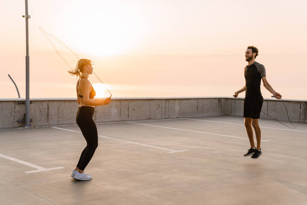 Young man and woman working out together with jumping ropes on parking outdoors - Foto, Bild