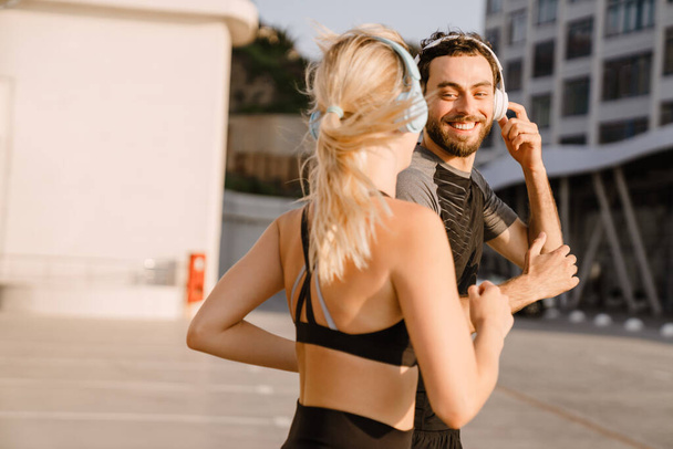 Young man and woman in headphones running together on parking outdoors - Fotografie, Obrázek
