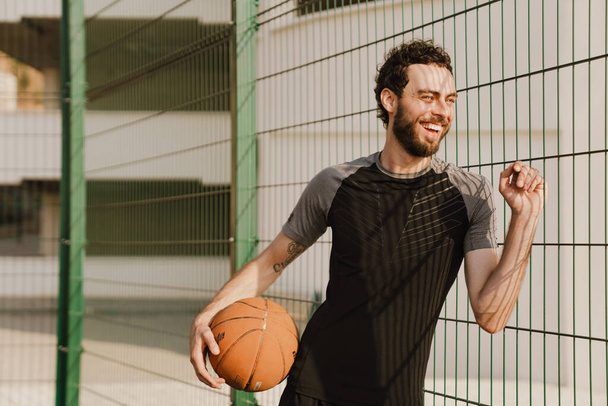Young white man smiling while working out with ball on sports ground outdoors - Foto, Imagen
