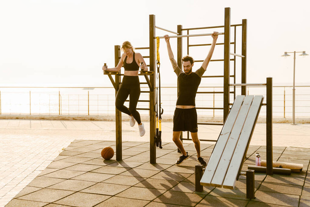 Young man and woman working out together on sports ground outdoors - Foto, Imagen