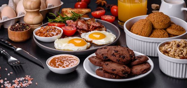 Ein leckeres gesundes Frühstück mit Spiegeleiern, Speck, Bohnen, einem Glas Saft, Haferkeksen, Milch und Marmelade. Gesunde Ernährung am Anfang des Tages - Foto, Bild