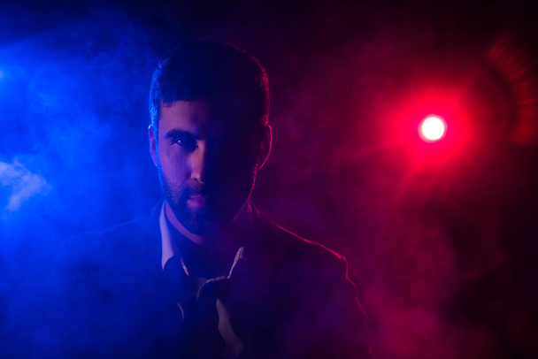 Photo of man looking at camera on dark background with pink and blue lights. - Fotó, kép