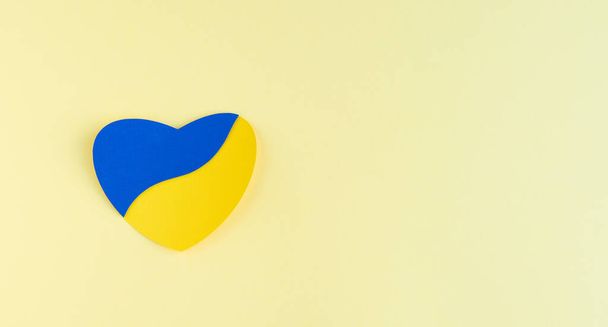 Heart cut out of paper with Ukrainian flag colors on yellow background. Copy space. - Foto, Bild