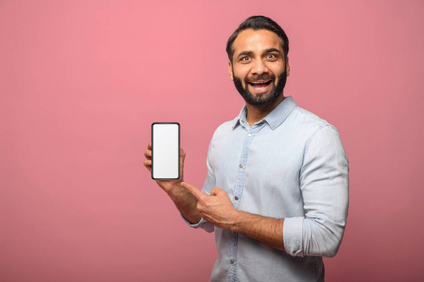 Surprised Indian man holds smartphone in a hand and points finger at empty phone screen - Photo, Image