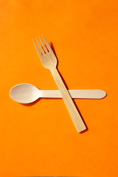 Cuchara de madera eco bambú y tenedor sobre fondo naranja brillante. Concepto de hora de comer - Foto, Imagen